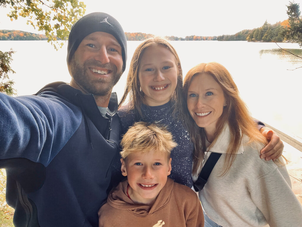 Family standing together outdoors near a lake during the fall season, reflecting the community and family values behind Legacy Hoops.